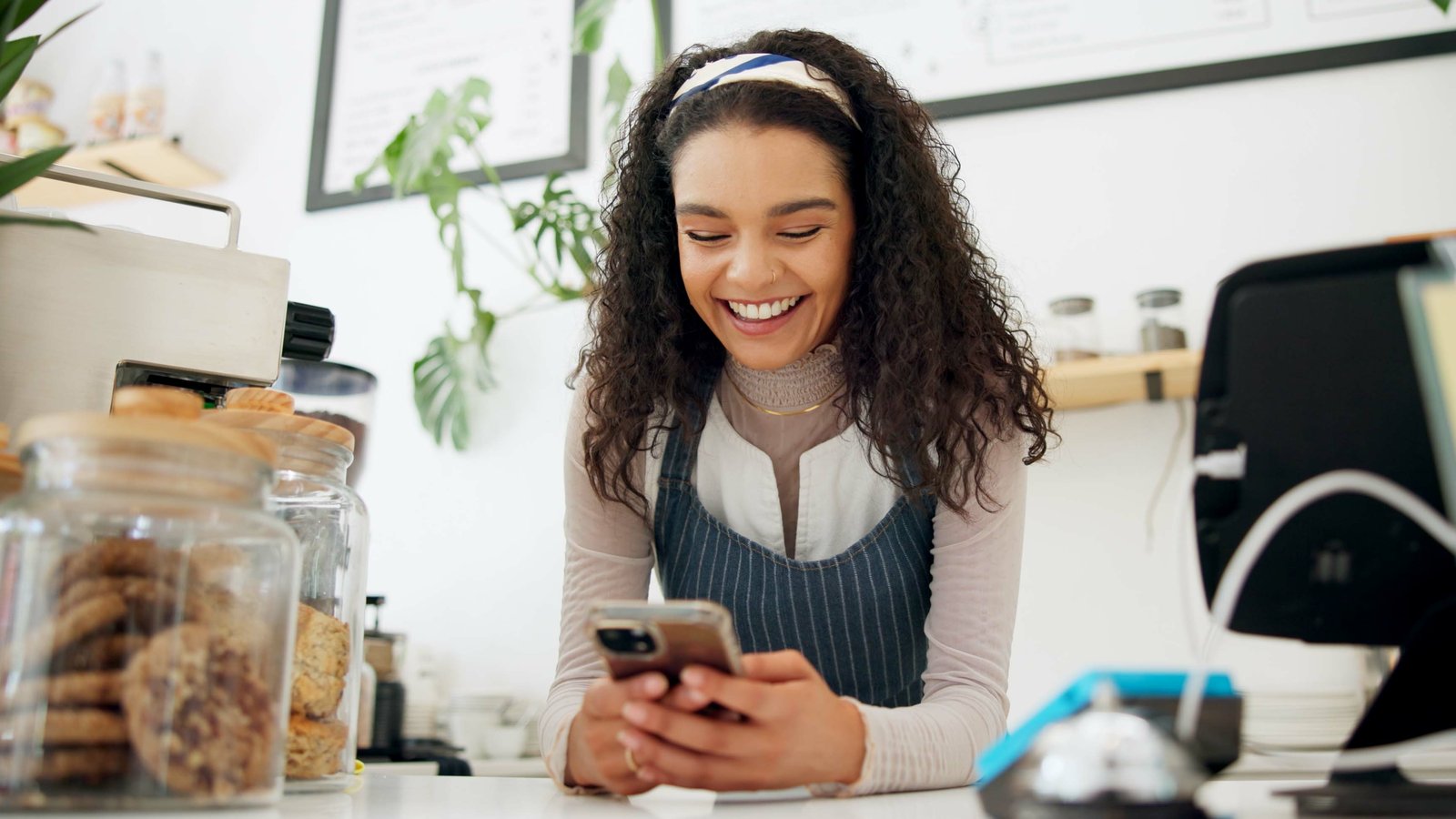 5 errores al vender por WhatsApp que te cuestan clientes Dueña joven de una panadería responde un mensaje en su celular, sonriendo detrás del mostrador