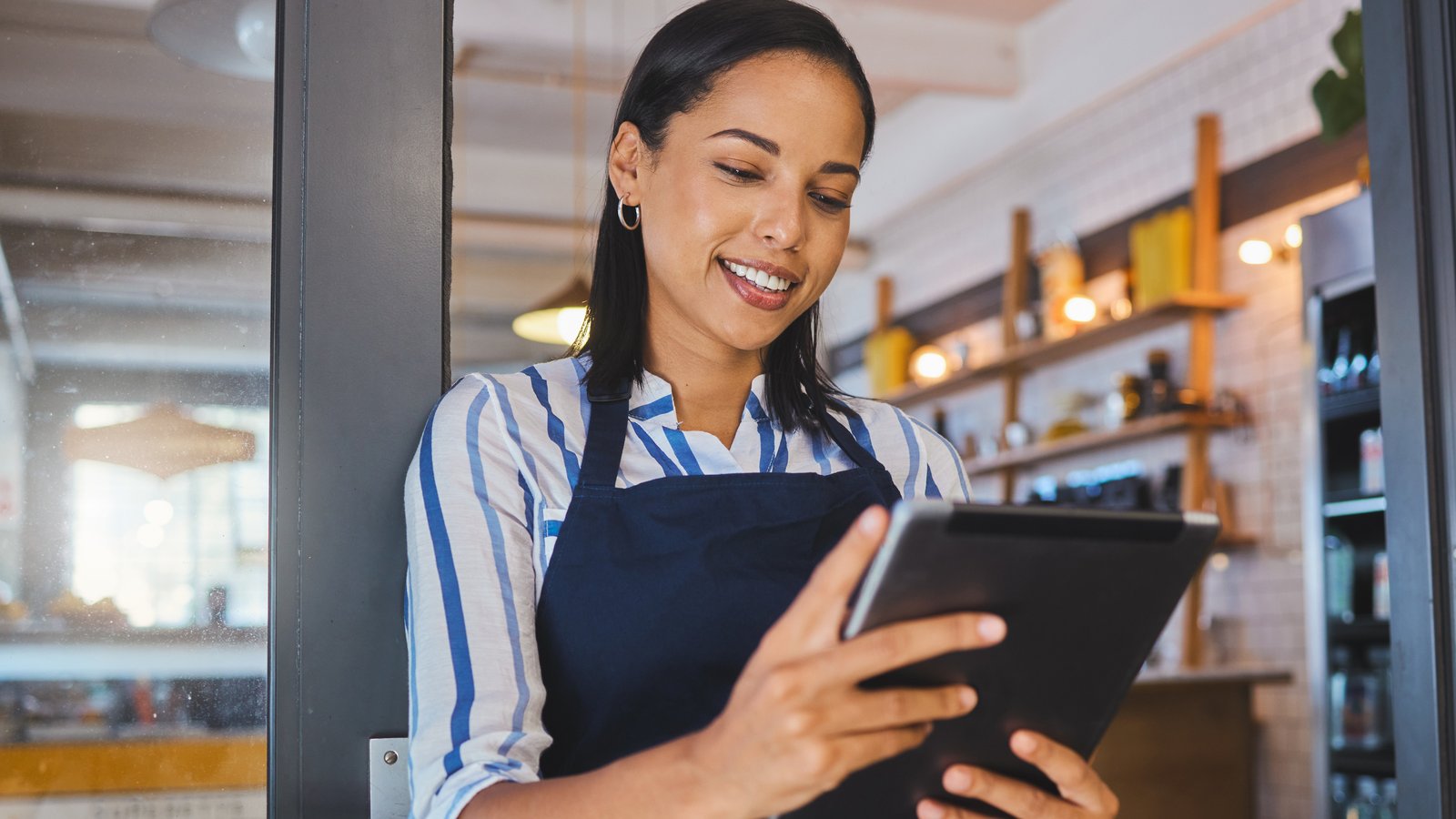 Cómo crear tu primera campaña en Facebook e Instagram, paso a paso Joven dueña de un café revisa los números de su negocio en una tableta, en la puerta de su local